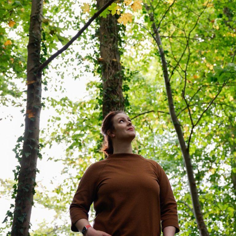 Katharina Perspektive Katharina steht zwischen dünnen hohen Bäumen mit hellgrünen Blättern und schaut nach oben